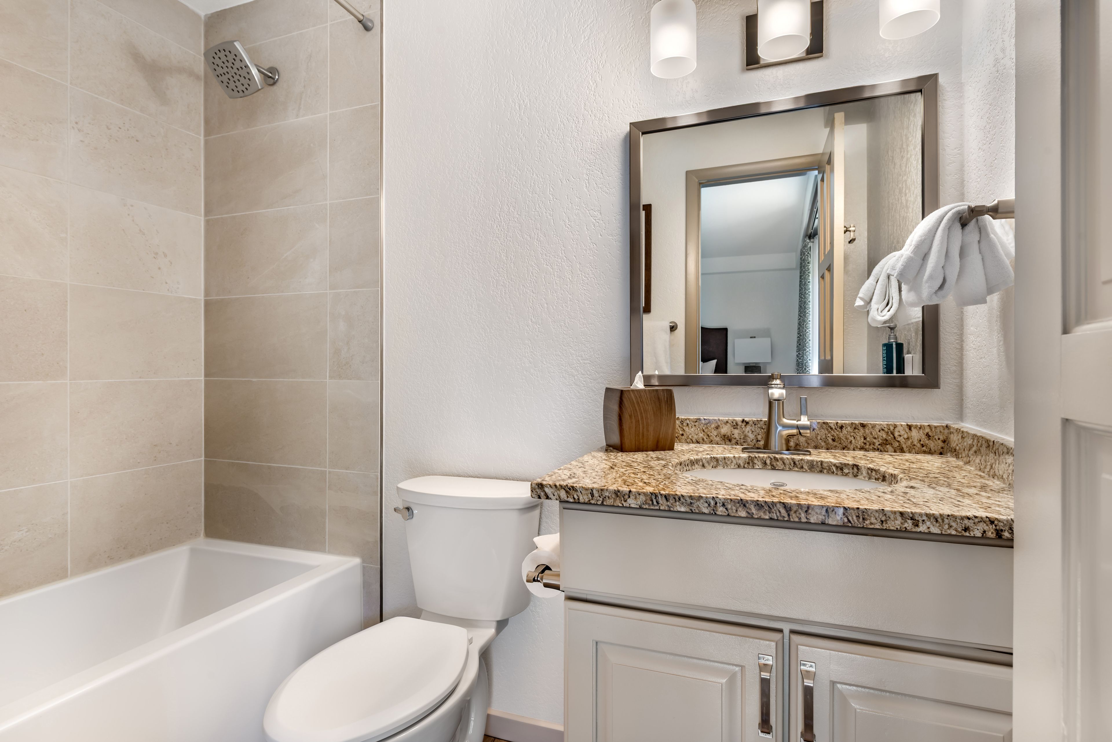 A bathroom with a bathtub, toilet, and vanity with a mirror.