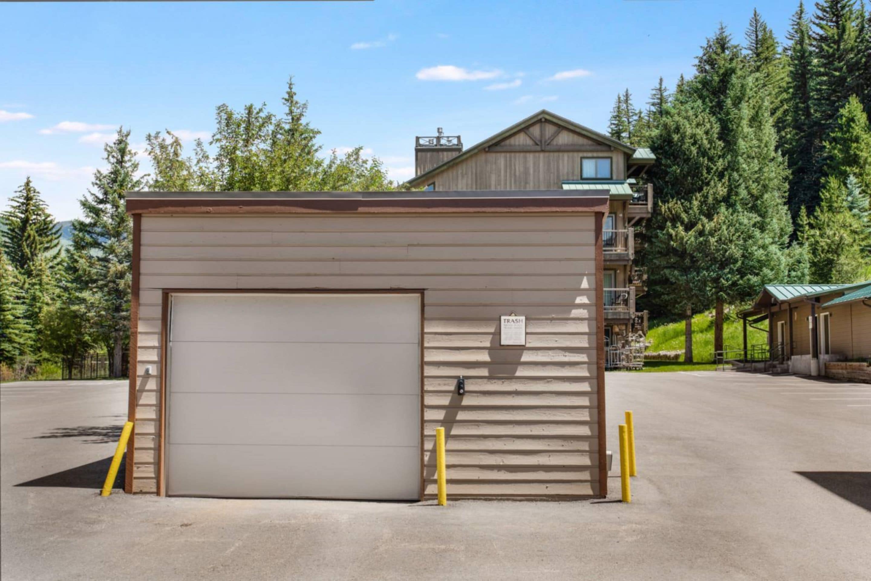 A single-story building with a garage door, surrounded by trees and a clear sky.