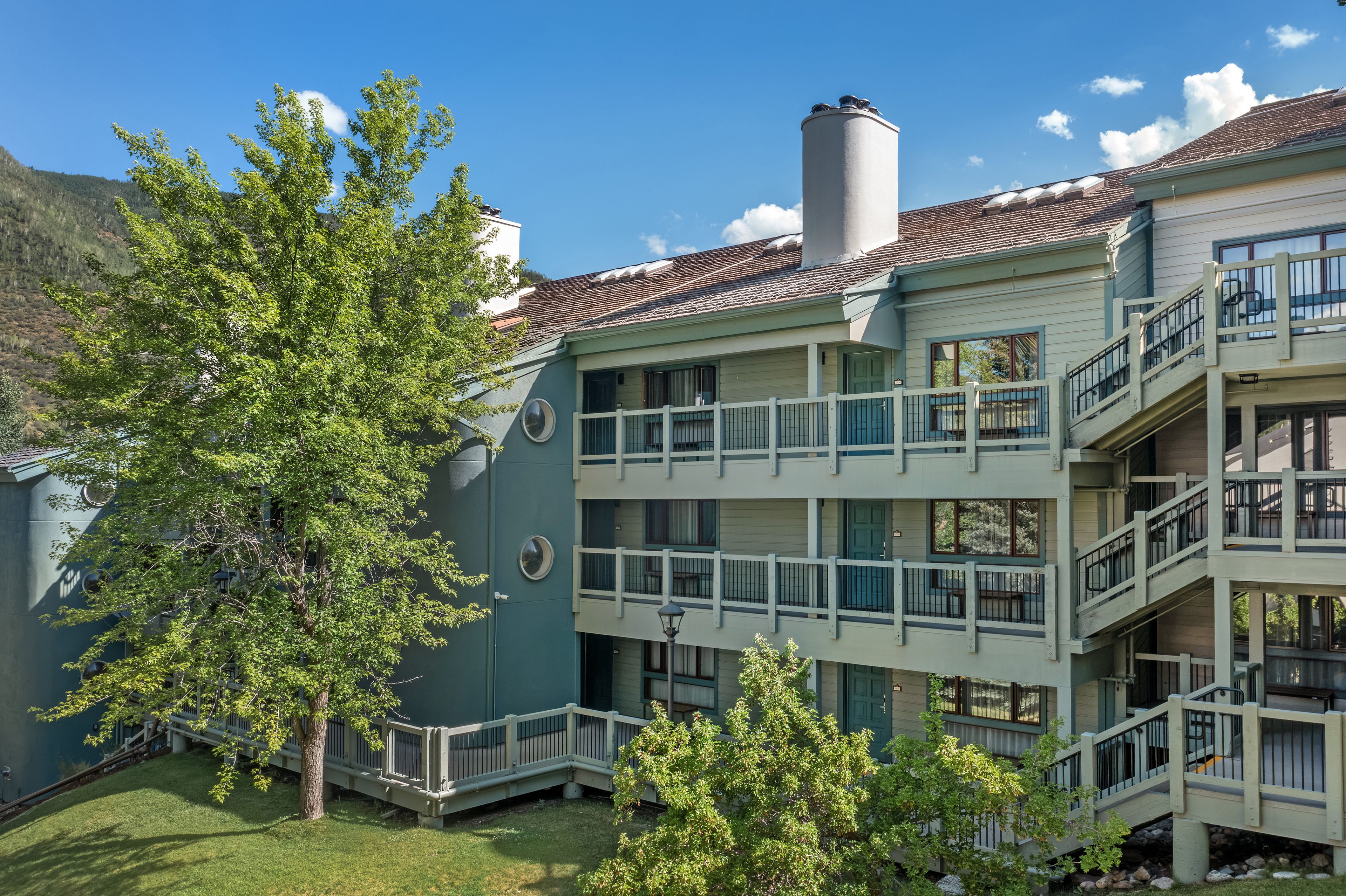 A multi-story hotel with balconies, a chimney, and a view of a mountain.