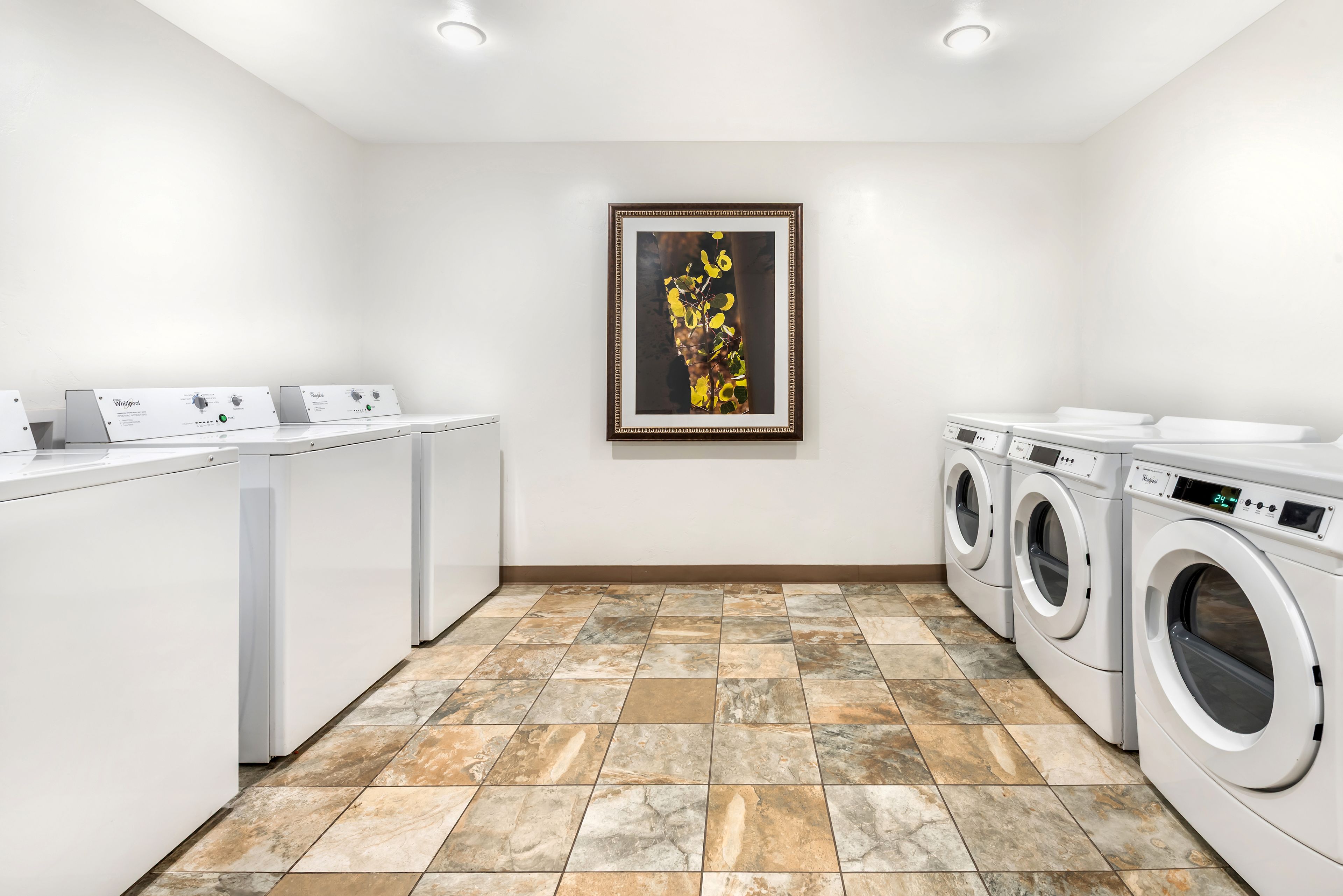 A laundry room with a tiled floor, a large framed artwork, and two Whirlpool washing machines.