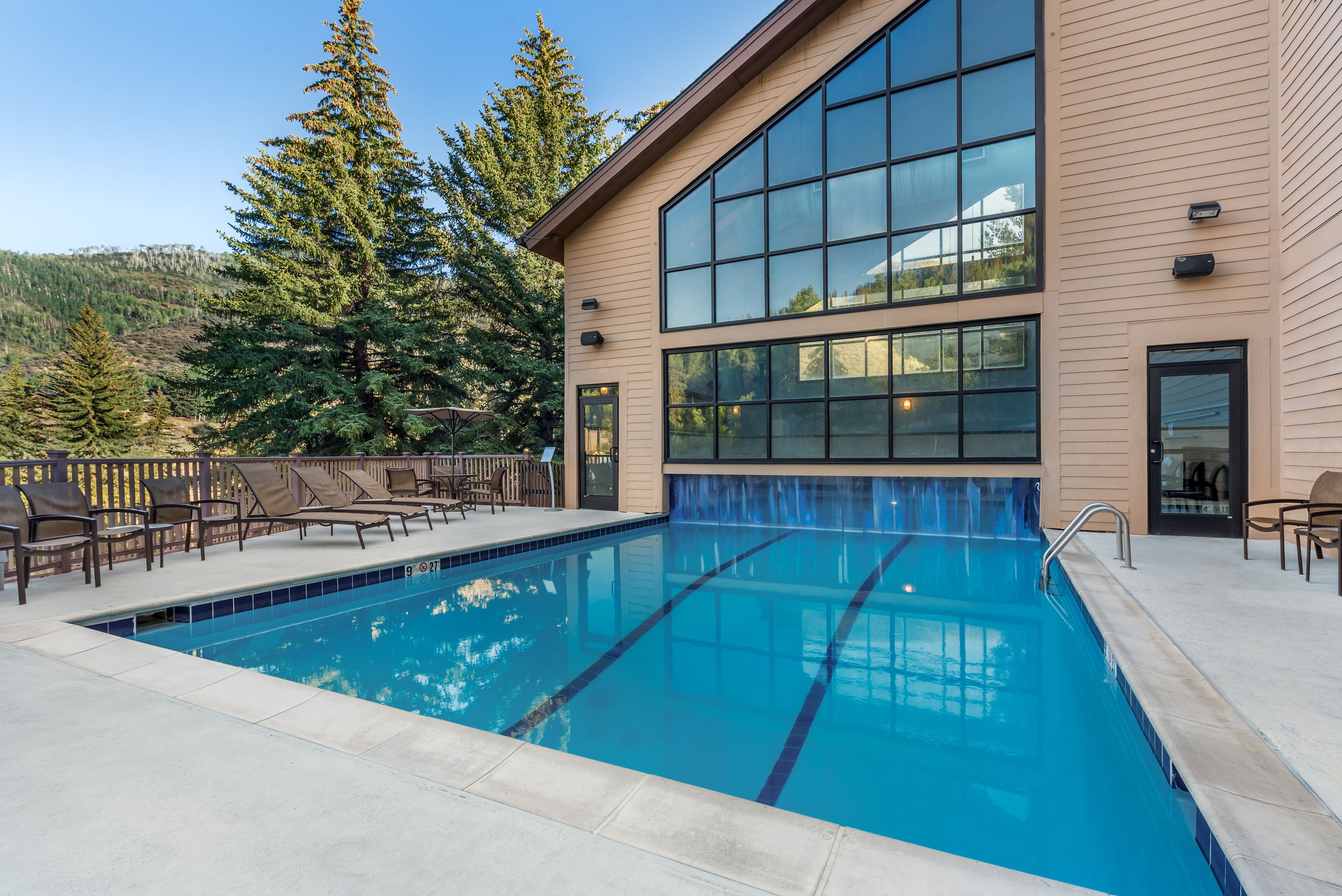 A swimming pool with a clear blue water, surrounded by lounge chairs and a wooden deck.
