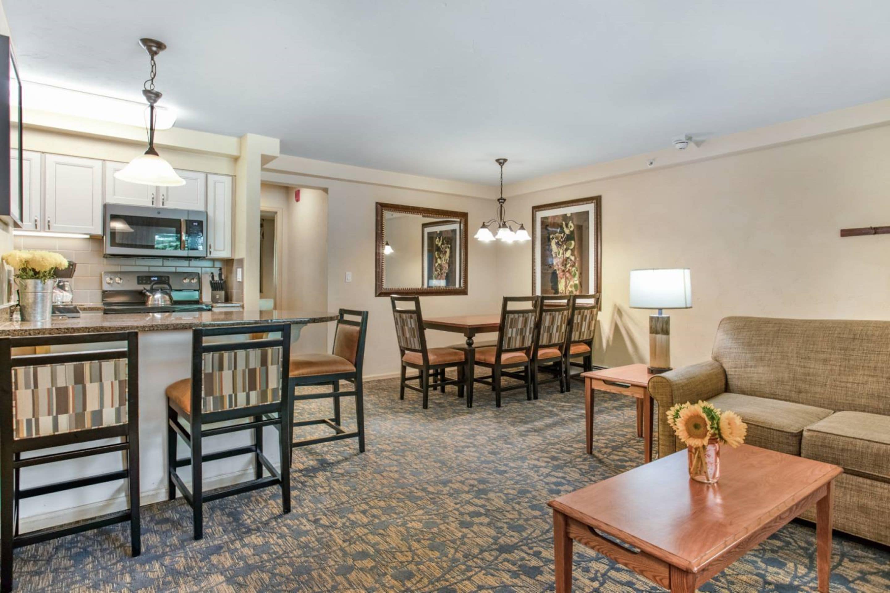 A hotel room with a kitchenette, dining area, and a living space with a sofa and coffee table.