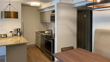 Een kleine keuken met een koffiezetapparaat, broodrooster en oven, een eettafel met stoelen, en een hangende lamp.