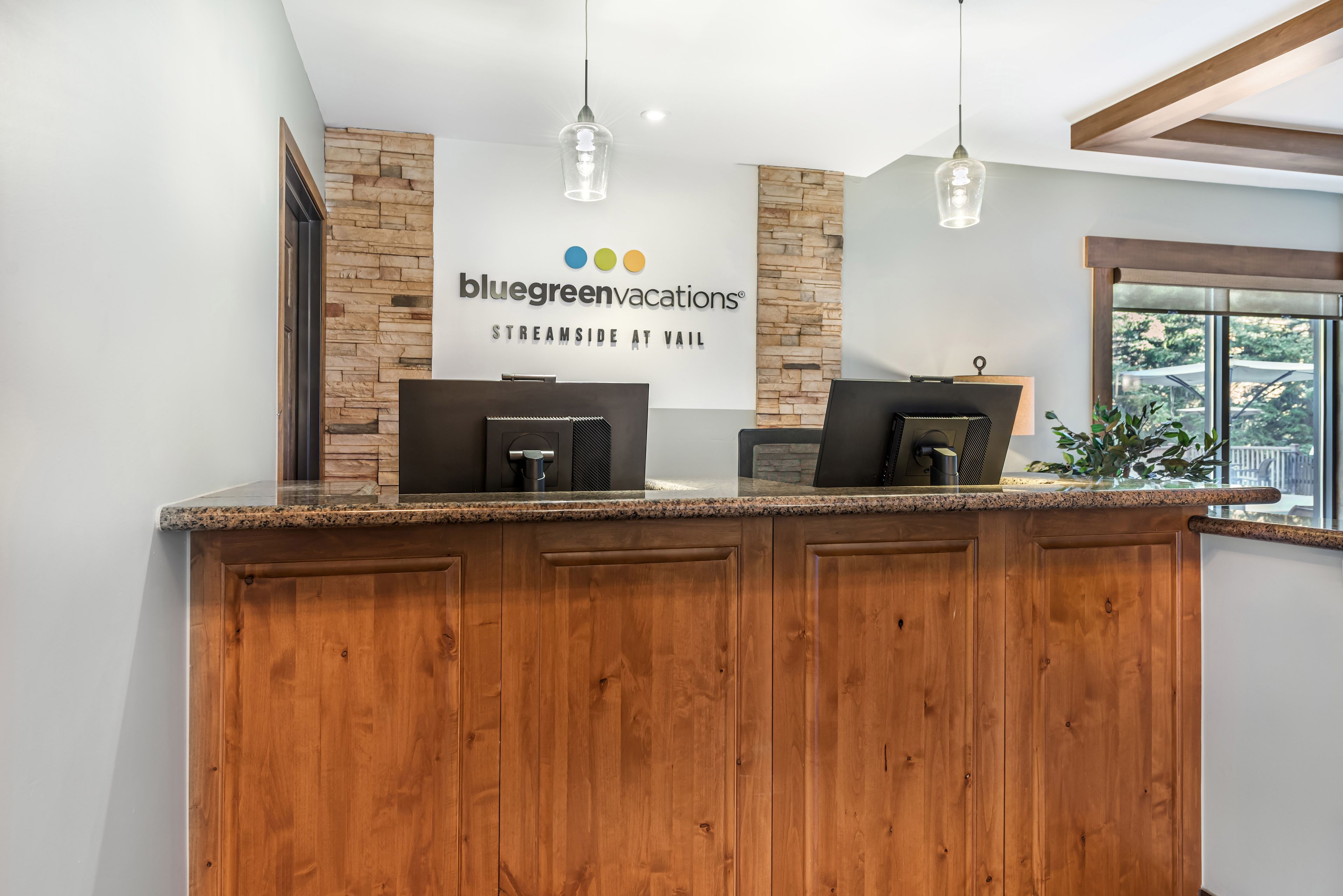 Een receptiebalie met een stenen achtergrond, een bord met daarop Bluegreen Vacations, en een raam met uitzicht.