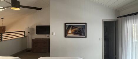 A room with two beds, a ceiling fan, a flat-screen TV, a wooden dresser, and a framed welcome sign.