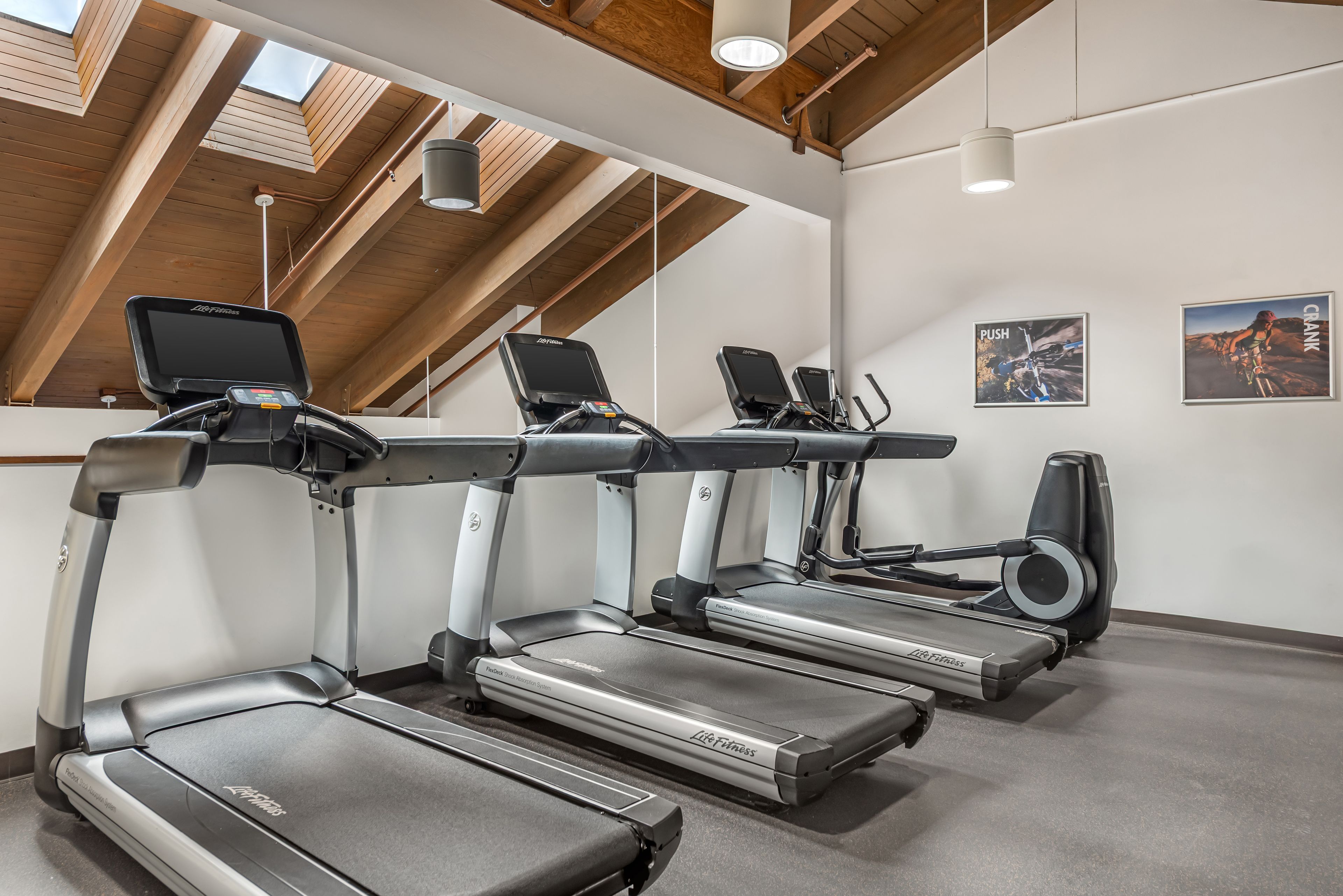 Un gimnasio con tres cintas de correr, un televisor en la pared y un cartel de un ciclista.