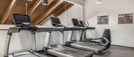 A gym with three treadmills, a wall-mounted TV, and a poster of a cyclist.