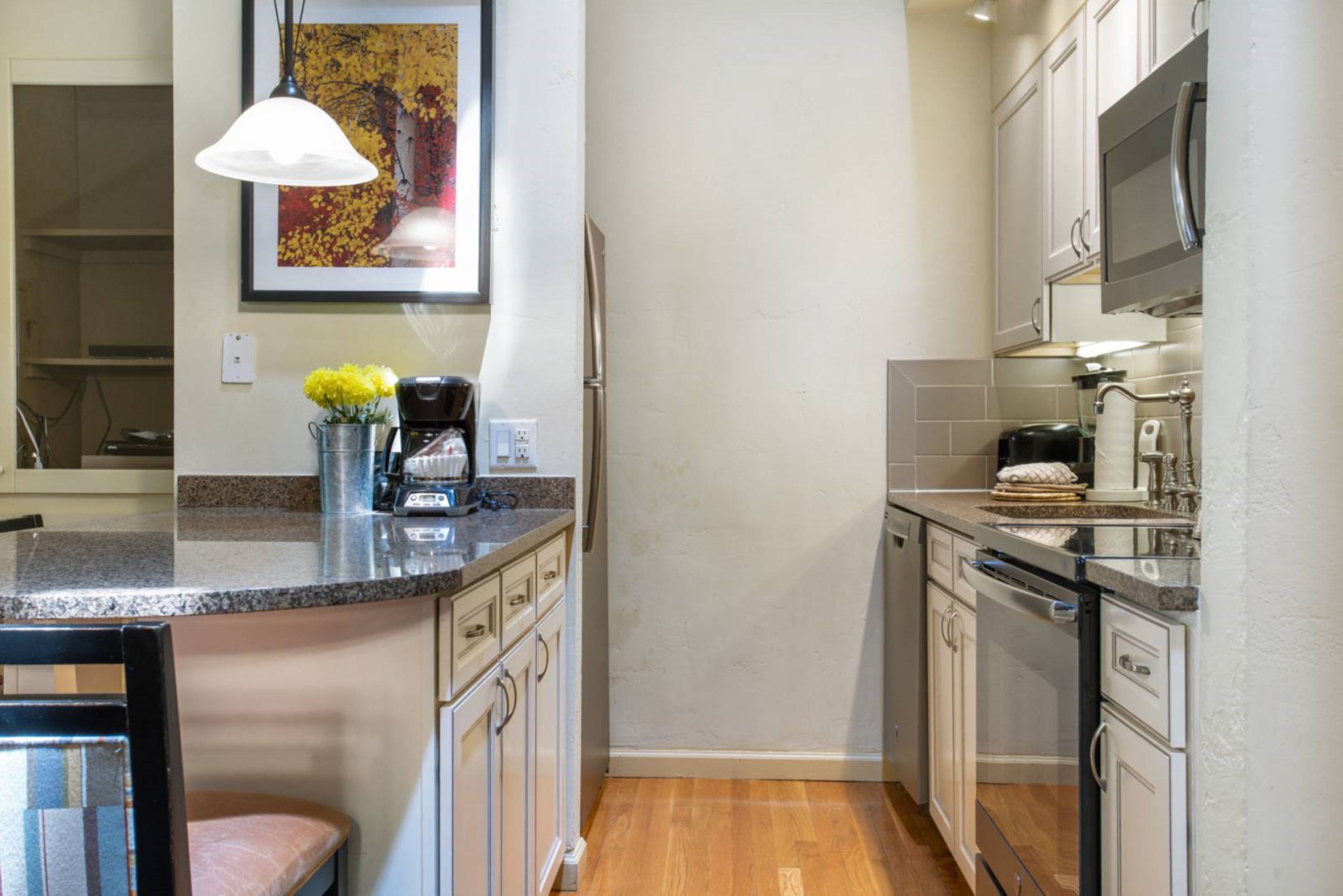 A kitchen with white cabinets, a granite countertop, a coffee maker, and a microwave.