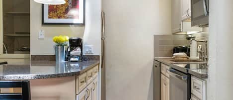 A kitchen with white cabinets, a granite countertop, a coffee maker, and a microwave.