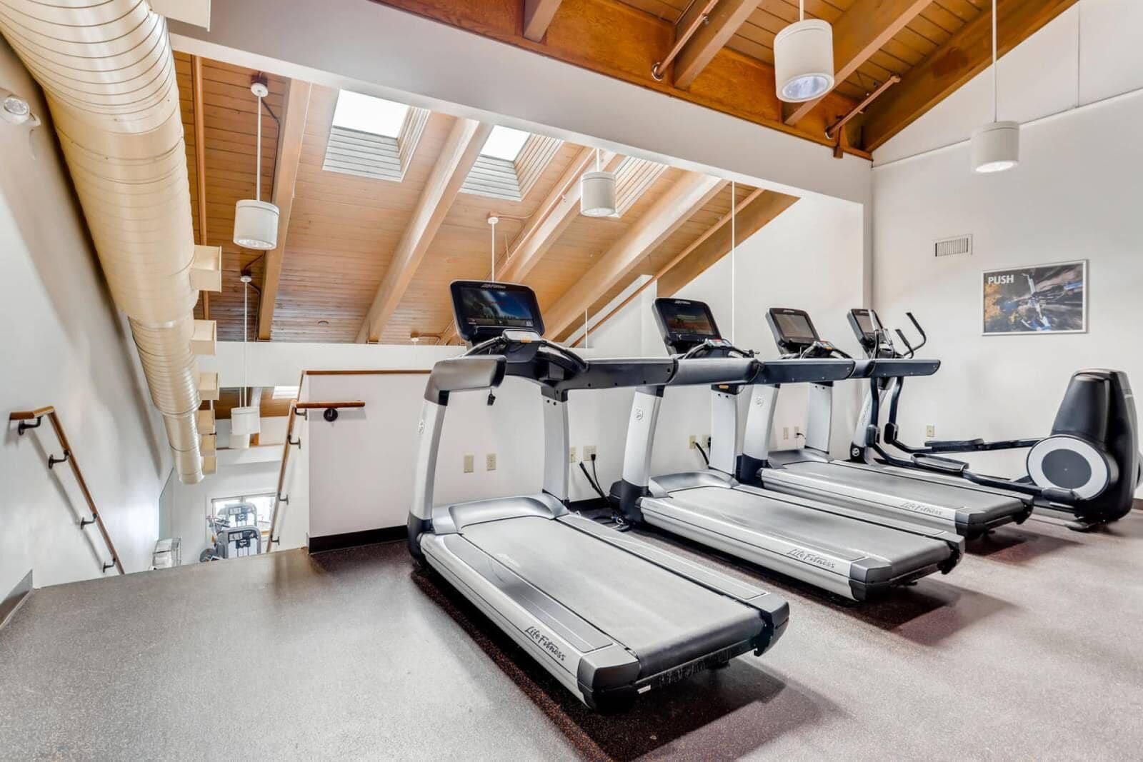 Un gimnasio con cintas de correr, elípticas y un espejo grande.
