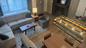 A modern living room with a sofa, a plaid armchair, a glass-top dining table, a fireplace, and a television. - Bluegreen Vacations Streamside at Vail, an Ascend Collection Resort (Vail)