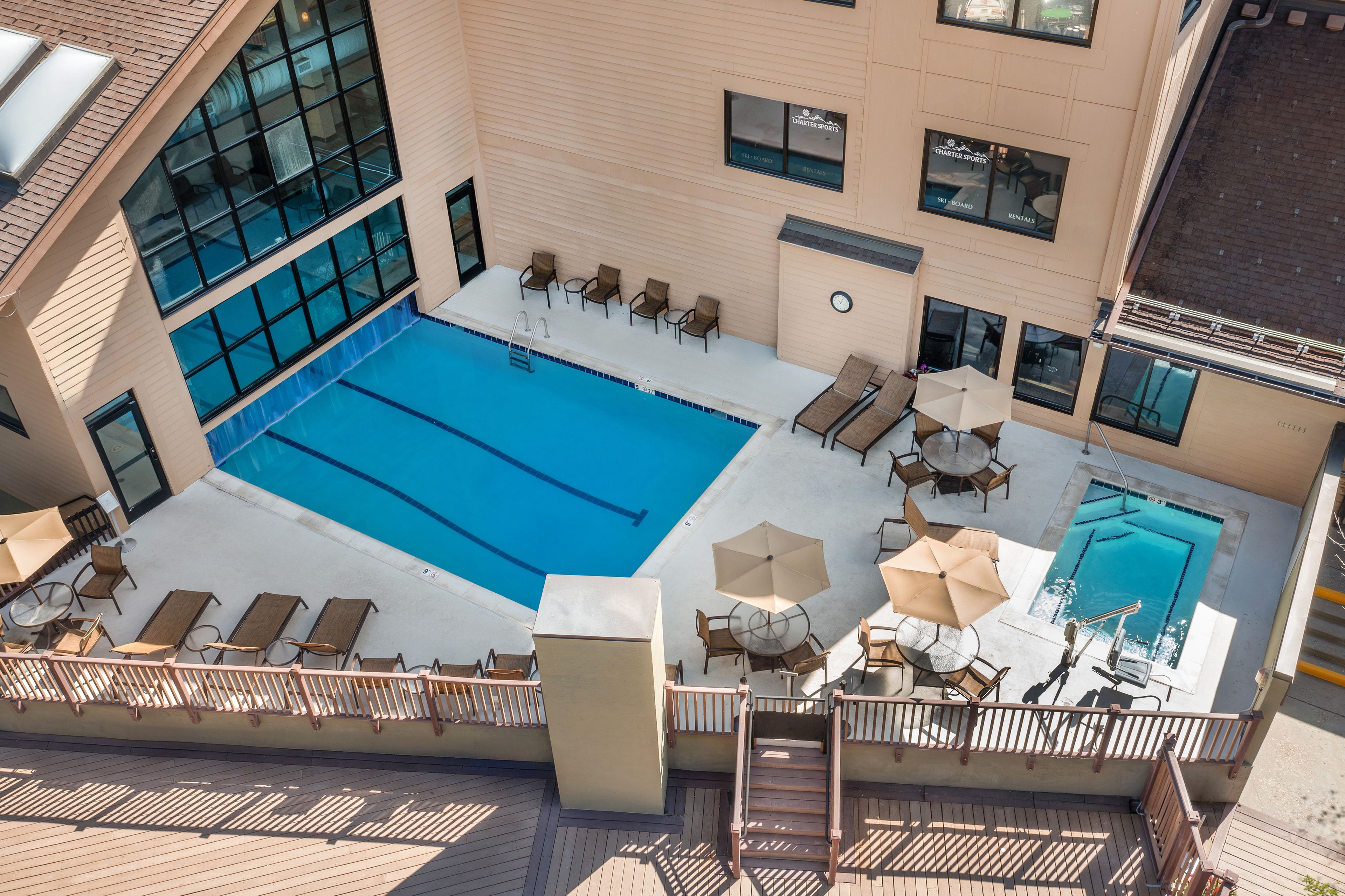 Un espace piscine aménagé sur le toit, doté de plusieurs chaises longues et de parasols, entouré d’une terrasse en bois et d’une balustrade en verre.