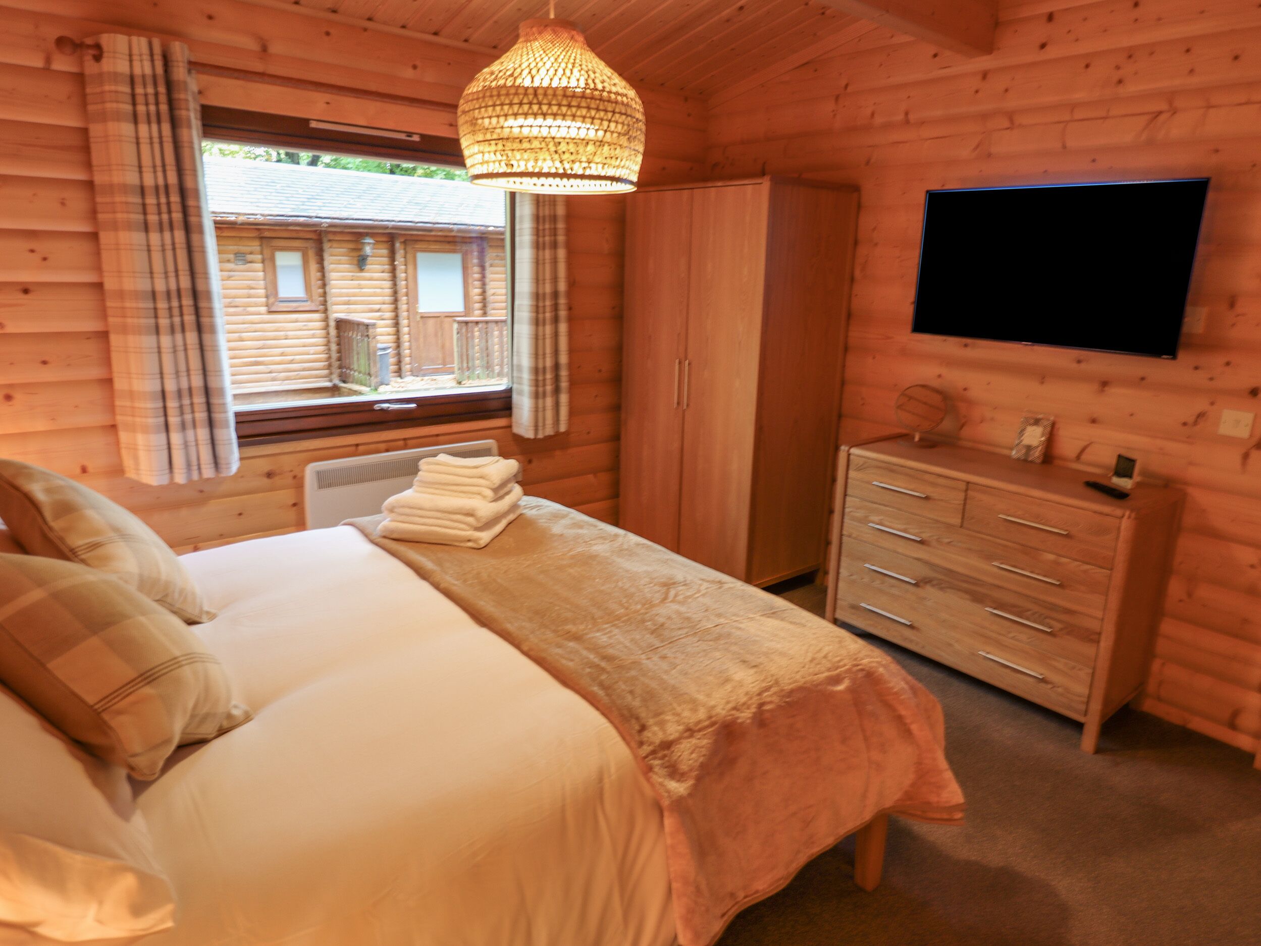 Une chambre confortable, aménagée dans un chalet en bois, avec un lit, une commode, un téléviseur et une fenêtre avec des rideaux.