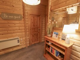 Interior de una cabaña de madera con un cartel que dice 'Sean nuestros invitados', una estantería llena de libros, una lámpara y una guía de Lincolnshire sobre la mesa.