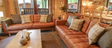 Interior acogedor de una cabaña con dos sofás de cuero, una mesa de centro de madera y un comedor con sillas y mesa de madera.
