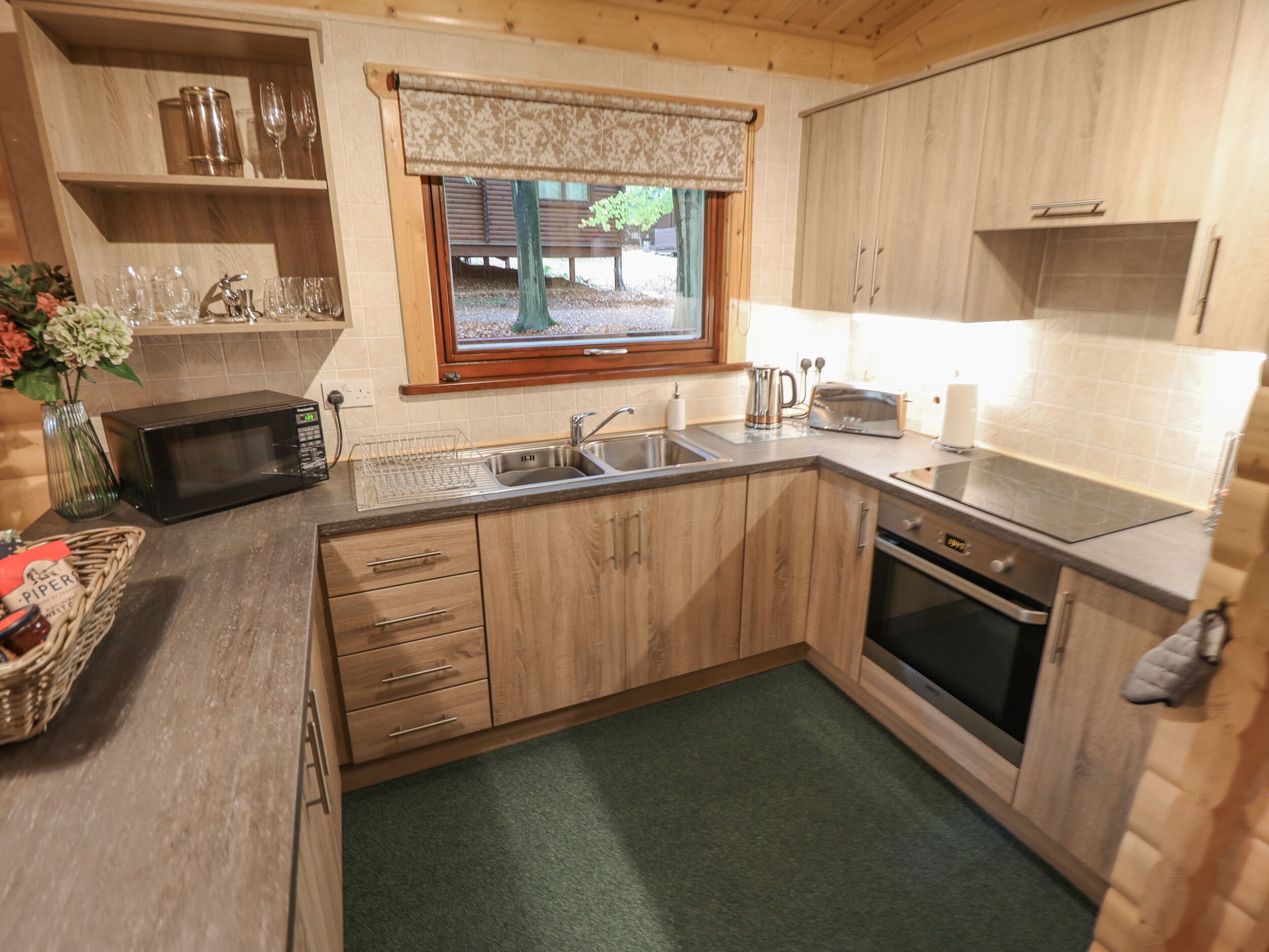 Cocina compacta con armarios de madera, microondas, lavaplatos y ventana con vistas al exterior.