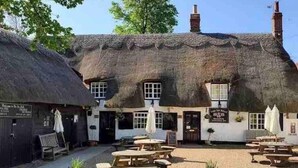 A traditional thatched-roof building with multiple windows and a signboard, surrounded by outdoor seating areas and potted plants. - Cottage in Area of Outstanding Natural Beauty (Didcot)