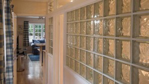A hallway with a glass block wall, a seating area with a sofa and table, and a door leading to another room. - Cottage in Area of Outstanding Natural Beauty (Didcot)