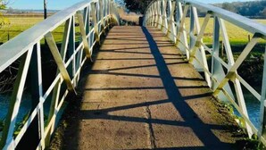 Een voetgangersbrug met witte hekken en een betonnen pad, dat uitkomt op een weids uitzicht over een natuurlandschap.
