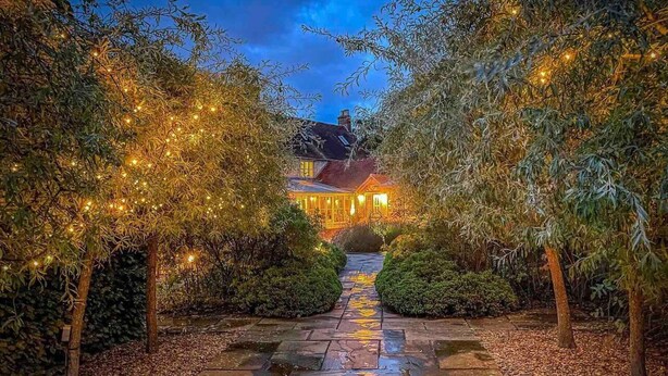 A pathway leading to a building with string lights and a wet ground. - Cottage in Area of Outstanding Natural Beauty (Didcot)