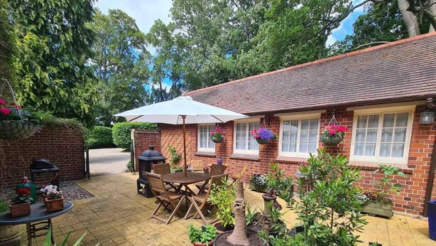 Een terras met een stenen huis, een ronde tafel met stoelen, een barbecue en potplanten.