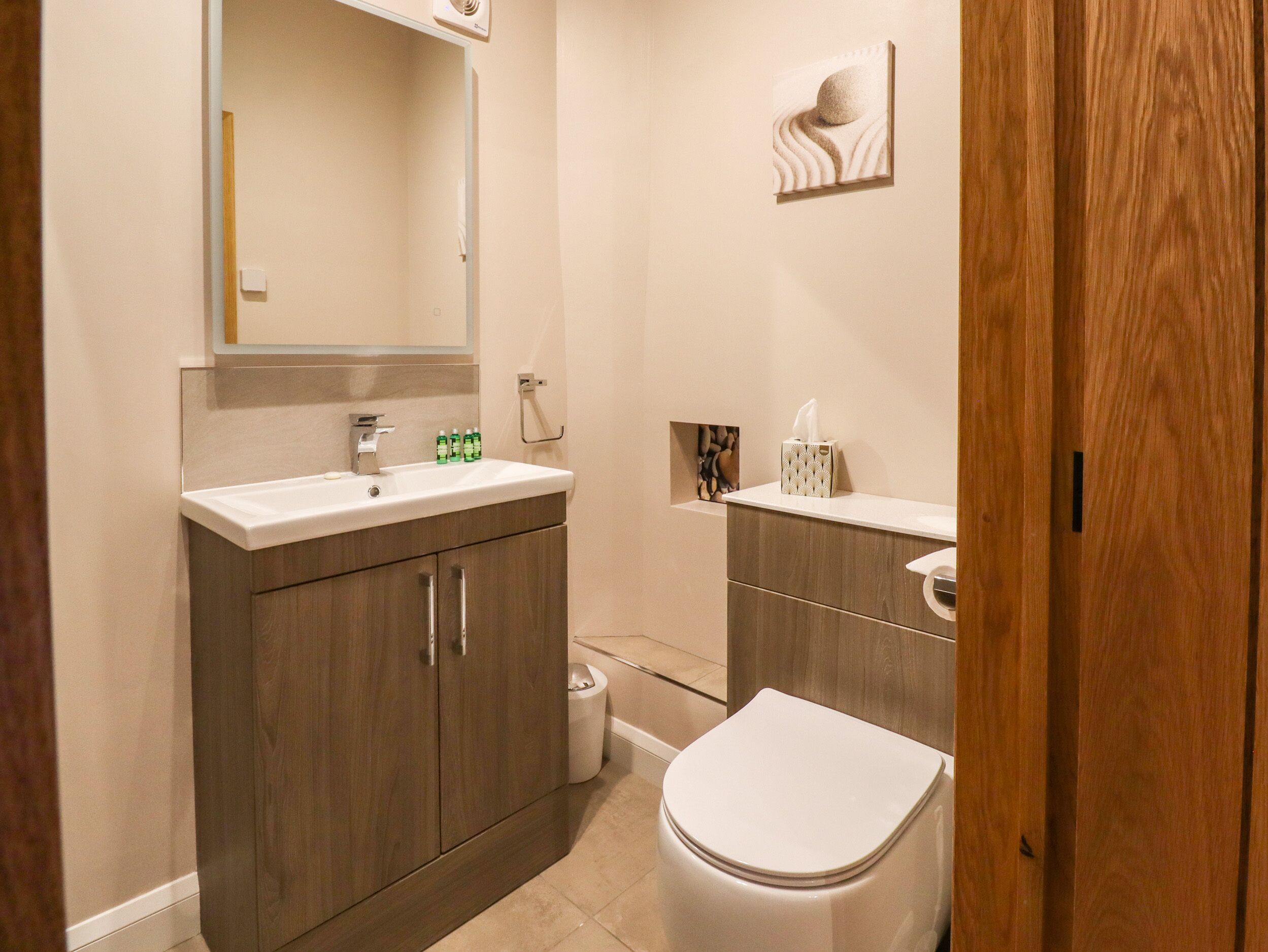Un baño moderno con un mueble de tocador de madera, un lavabo, un inodoro y un espejo.