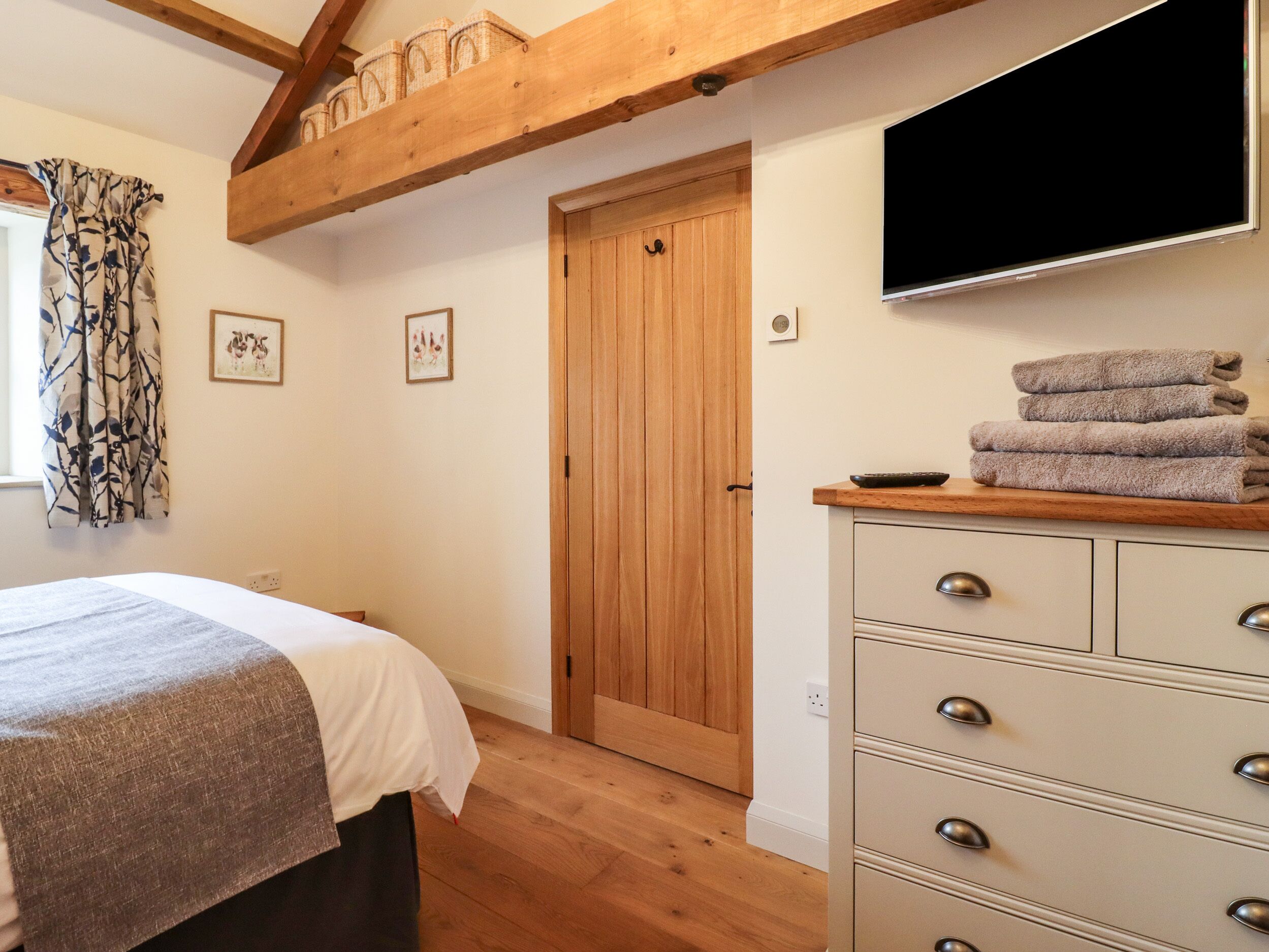 A bedroom with a bed, wooden ceiling beams, a TV, a dresser, and a door.