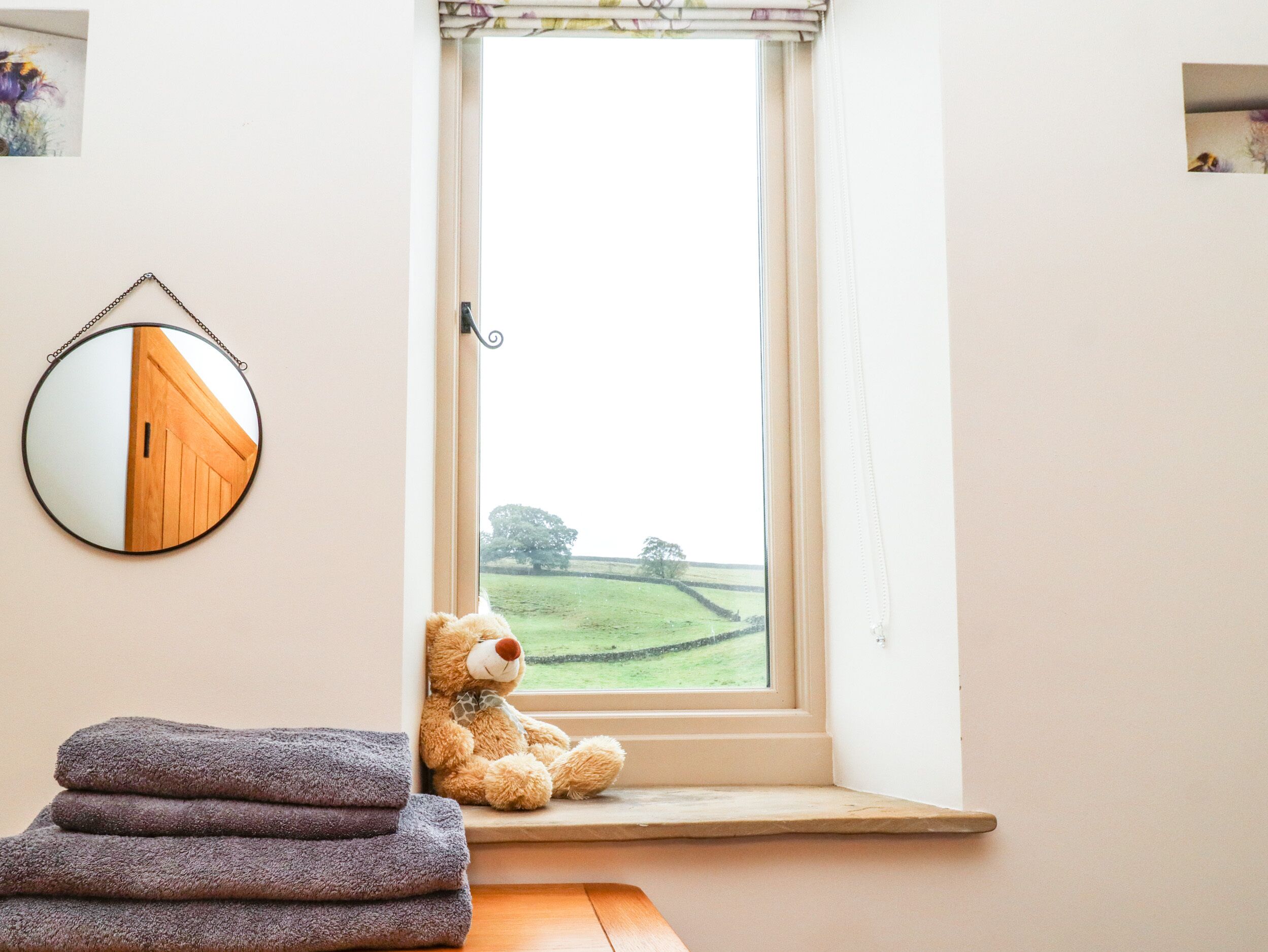 Um quarto com janela, um urso de pelúcia e um espelho refletindo uma porta.