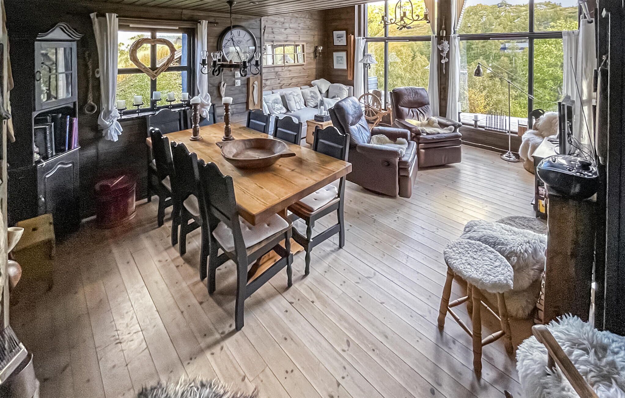 Een gezellig, landelijk interieur met een houten eettafel, lederen stoelen en een groot raam met uitzicht op groen.