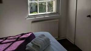 A room with a bed, a window with a view of buildings and trees, and a radiator.
