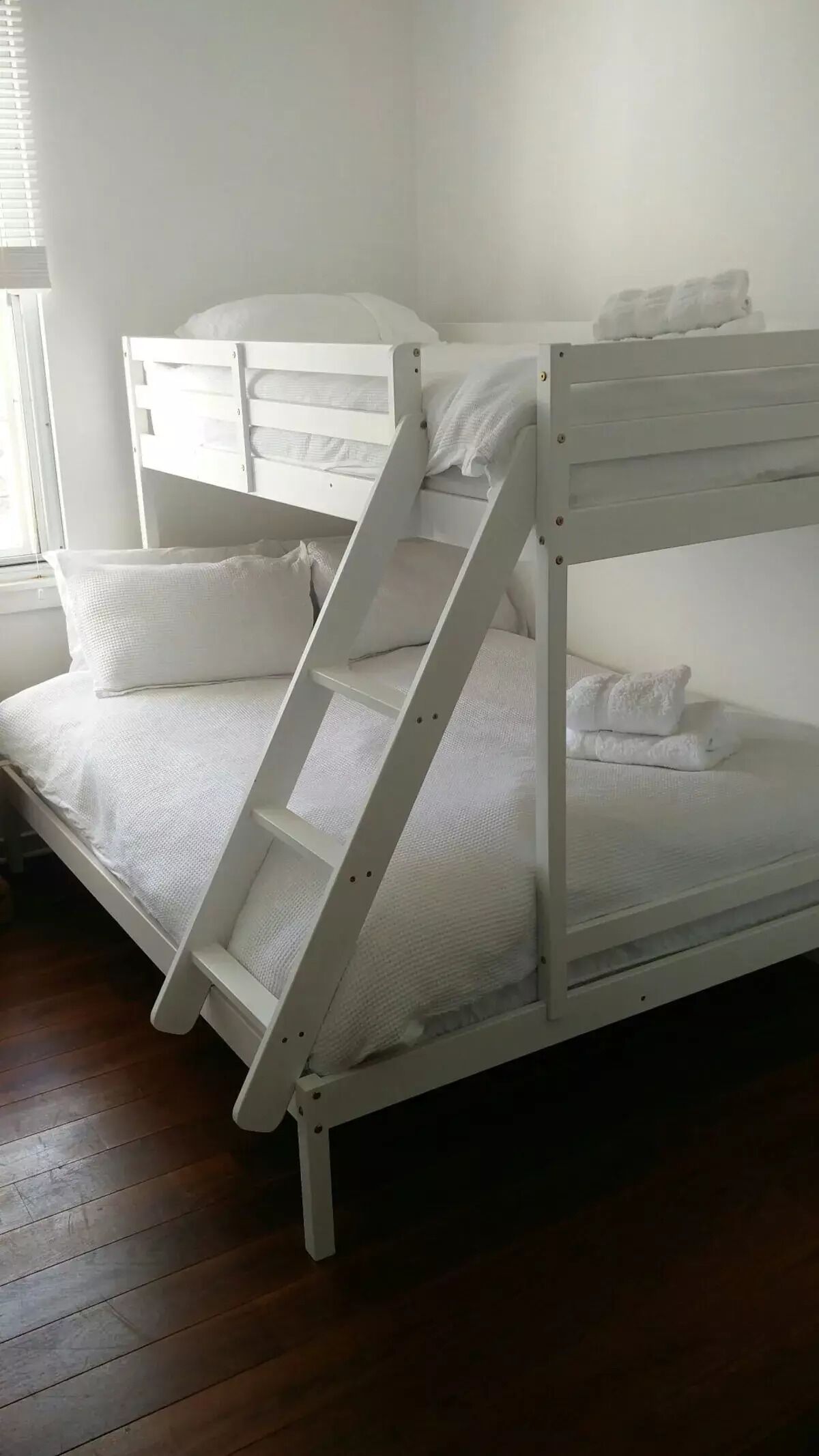 A bunk bed with a ladder, white bedding, and a window with blinds.