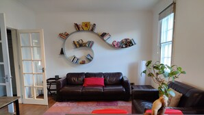 A living room with a dark leather sofa, a coffee table, and a bookshelf with books and decorative items.