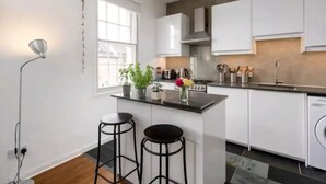 A modern kitchen with white cabinets, a central island with stools, a window, and a washing machine.