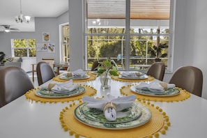 Enjoy meals in this beautifully set dining area with a long table, comfortable chairs, and a vase with fresh greenery.