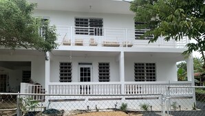 A two-story white building with a balcony, a small garden area with pebbles and plants, and a chain-link fence. - Elana's WhiteHouse. #3 Anasco PR. (Añasco)