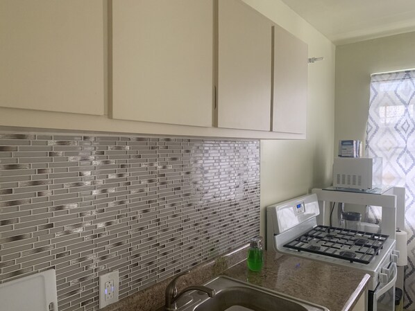 A kitchen with a tiled backsplash, a stainless steel sink, a gas stove, and a microwave. - Elana's WhiteHouse. #3 Anasco PR. (Añasco)