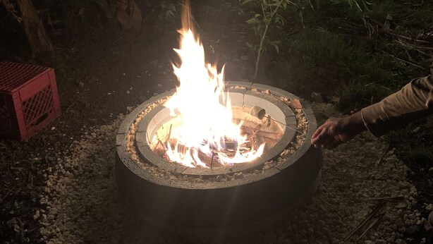 A circular fire pit with flames, surrounded by gravel and plants. - Elana's WhiteHouse. #3 Anasco PR. (Añasco)