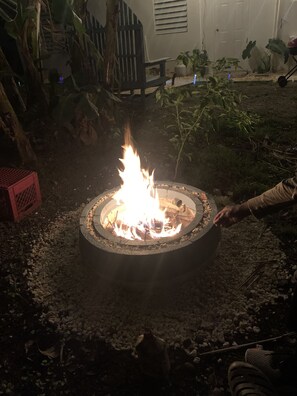A circular fire pit with flames, surrounded by gravel and plants. - Elana's WhiteHouse. #3 Anasco PR. (Añasco)