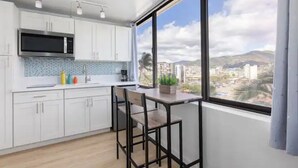 A modern kitchen with white cabinets, a black microwave, and a large window offering a city view. - King Bed/Renovated/Canal& Mountain View/Walk Beach (Honolulu)