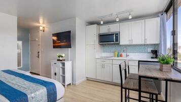 Cocina moderna con armarios blancos, un microondas y un lavamanos. Hay una mesa de comedor con sillas y una pequeña planta en maceta.