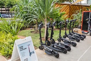 Una fila de scooters eléctricos alineados al aire libre, con un cartel en primer plano.