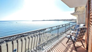 Un balcón con vista al mar, barandilla y dos sillas.