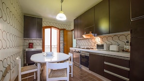 Una cocina con una mesa redonda de comedor, sillas blancas, una estufa, un tostador y una cafetera.