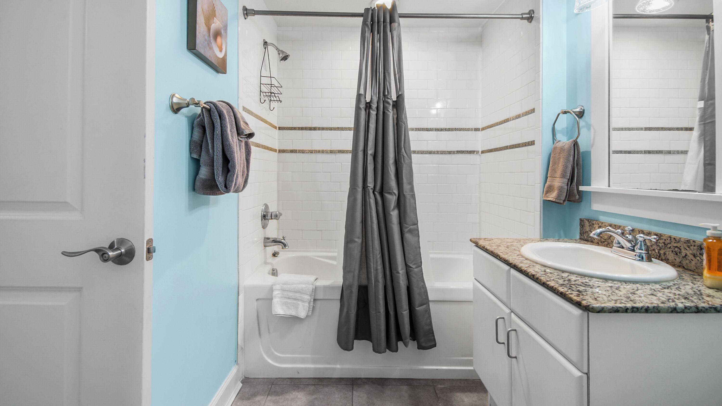 A bathroom with a bathtub, a shower curtain, a sink, and a mirror.