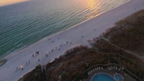 Vista a la playa con un atardecer, un muelle y una zona de piscina con tumbonas.