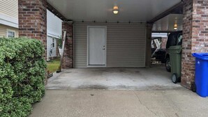 A covered parking area with a garage door, a brick wall, and a green bush. - Small Efficiency near Surfside Beach Pier (Surfside Beach)