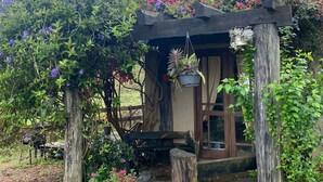Una estructura rústica de madera con un banco, rodeada de vegetación exuberante y plantas en flor.