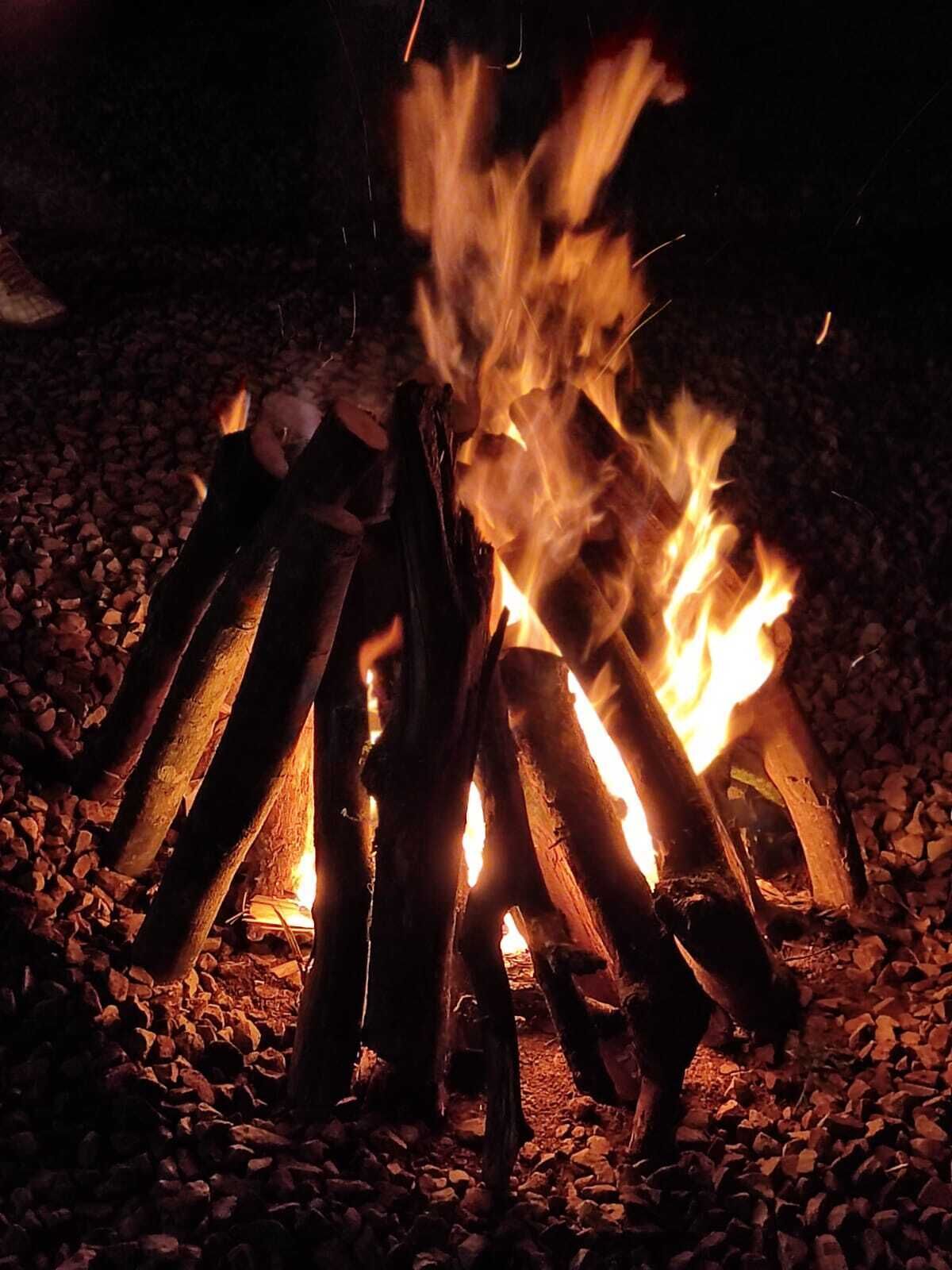 A campfire with logs arranged in a teepee shape, surrounded by gravel.