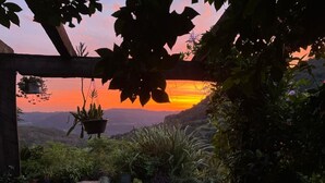 Un jardín con una pérgola de madera, plantas en macetas y vistas a un paisaje montañoso al atardecer.