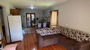 Un amplio espacio de sala con piso de madera, un sofá, una silla y un refrigerador.